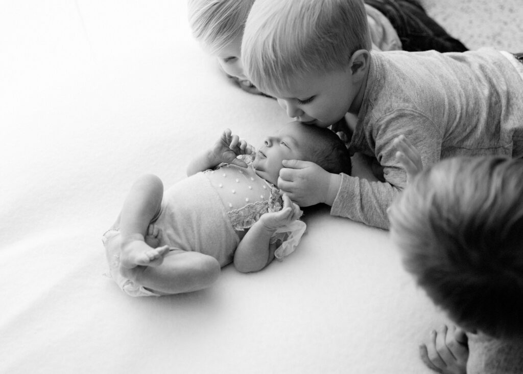Siblings of a newborn look over baby lovingly in an heirloom portrait image
